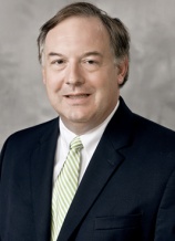 A man in suit and tie standing next to wall.