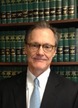 A man in suit and tie standing next to a book shelf.